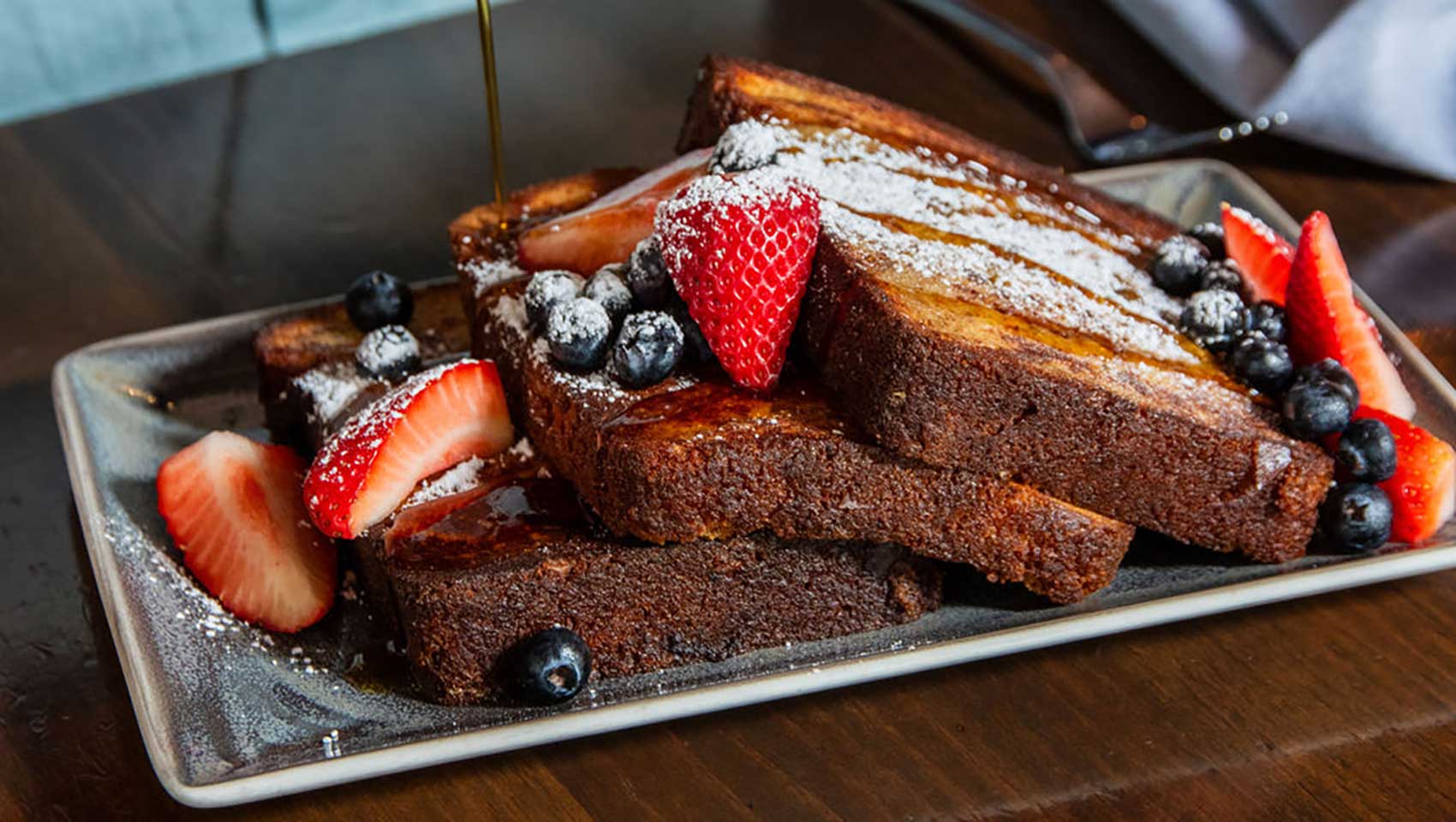Man's hand pouring syrup on french toast with assorted berries
