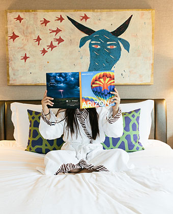 woman on bed is guestroom holding Arizona Magazine